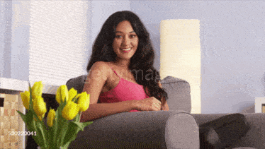 a woman in a pink tank top sits on a couch