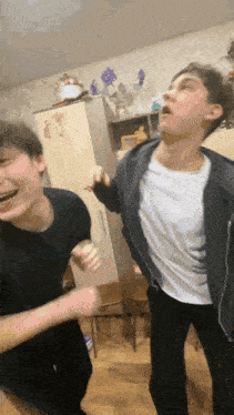 two young men are standing next to each other in a room laughing