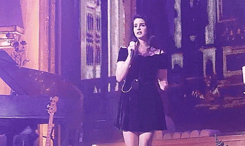 a woman in a black dress is singing into a microphone on stage