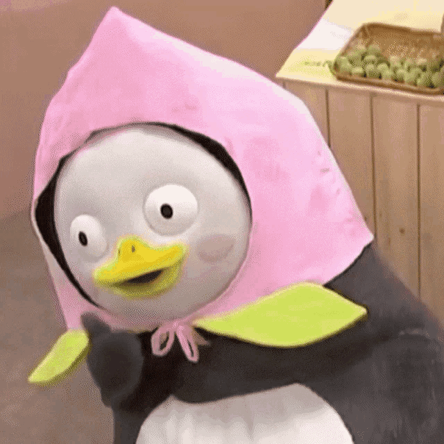 a stuffed penguin wearing a pink hat with green leaves on it .