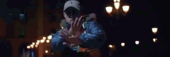 a man wearing a hat and sunglasses is standing in a dark room with lights behind him .