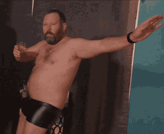 a shirtless man in leather shorts holds a glass