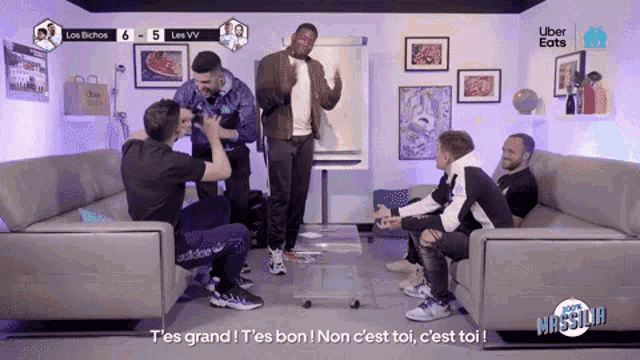 a group of men are sitting in a living room with uber eats in the corner