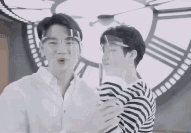 a man wearing a face shield is hugging another man in front of a clock .