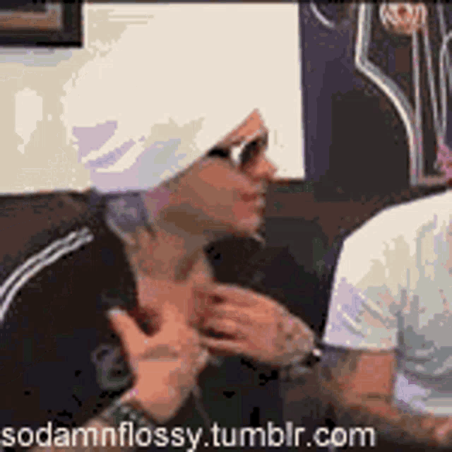 a man wearing a white hat and sunglasses is talking to another man in a room .