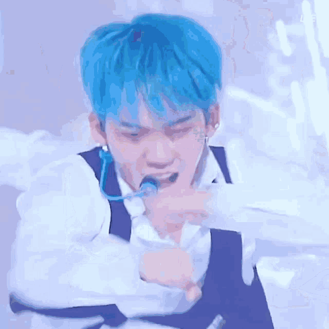 a man with blue hair and a microphone in his mouth is dancing on stage .