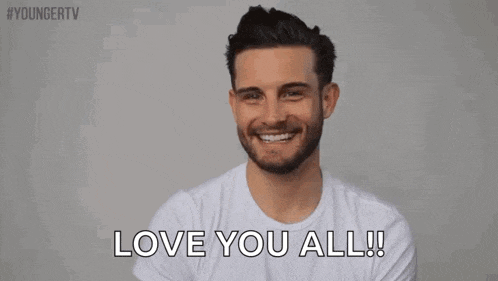 a man in a white t-shirt is smiling and saying i love you all .