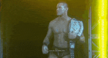 a shirtless wrestler is holding a championship belt in a dark room