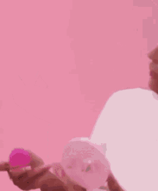a woman in a white shirt is holding a pink sponge in her hands .