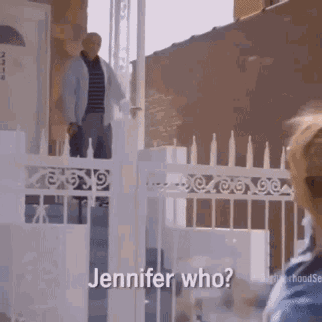 a man is standing in front of a white fence and talking to a woman .