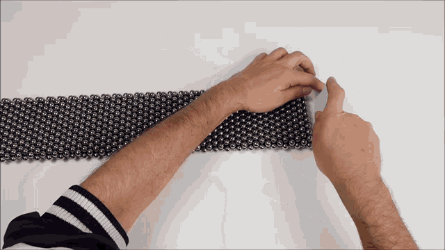 a man 's hands are playing with a row of balls on a white surface