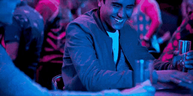 a man is sitting at a table in a bar holding a glass of beer and smiling .