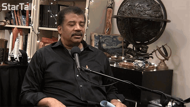 a man in a black shirt is sitting in front of a microphone with a startalk logo behind him
