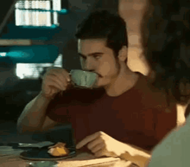 a man is drinking from a cup while sitting at a table with a woman .
