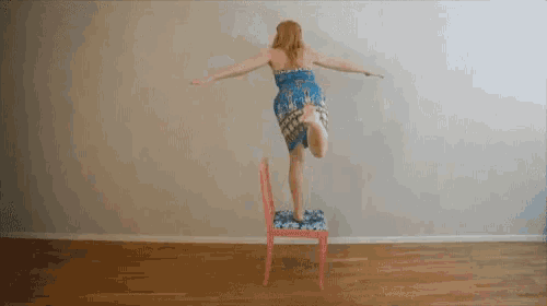 a woman in a blue dress stands on a pink chair
