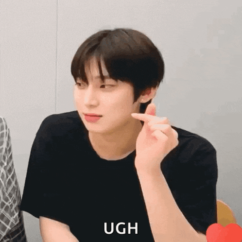 a young man is making a heart shape with his finger while wearing a black shirt .
