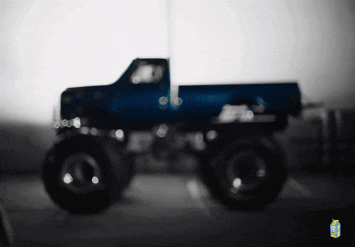 a blue monster truck is parked in a parking lot next to a bottle of lemonade