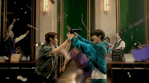 two men are playing with a hair dryer in a room with confetti flying