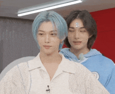 a boy with blue hair is standing next to another boy with long black hair .