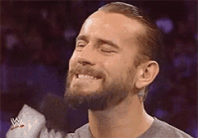 a man with a beard is smiling in front of a microphone with the word wwe on it .