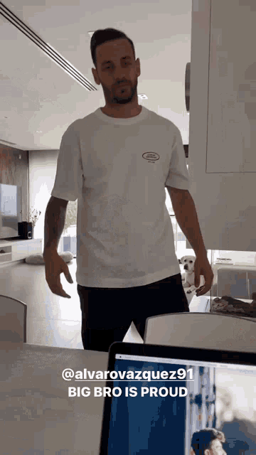 a man in a white t-shirt is standing in front of a laptop with the words big bro is proud below him
