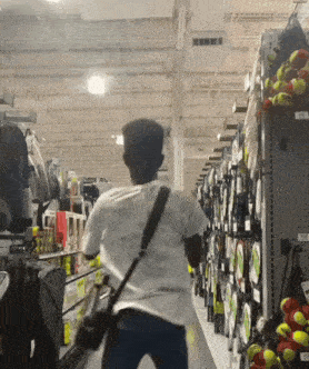 a man is walking down a aisle in a store with tennis balls hanging on the wall