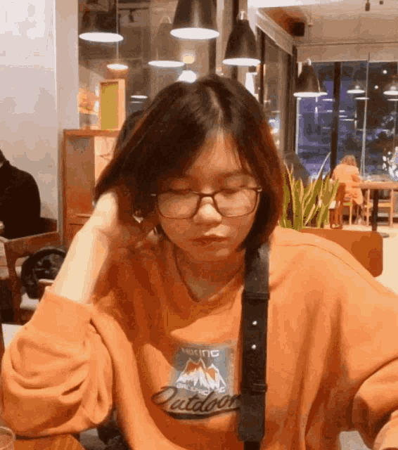 a girl wearing glasses and an orange sweatshirt with the word outdoor on it