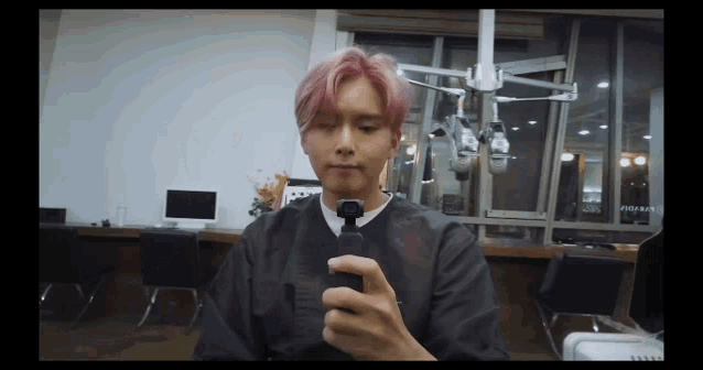 a man with pink hair is holding a cell phone