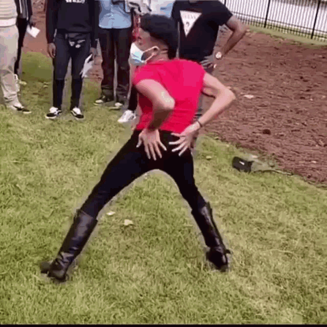 a woman in a red shirt and black pants is dancing on the grass .