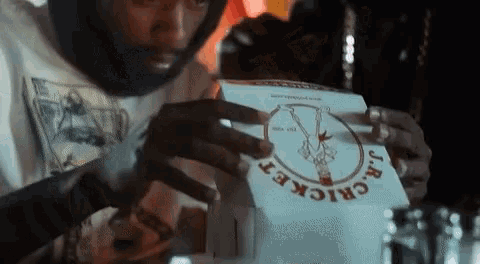 a man is opening a box of j.r. cricket pizza