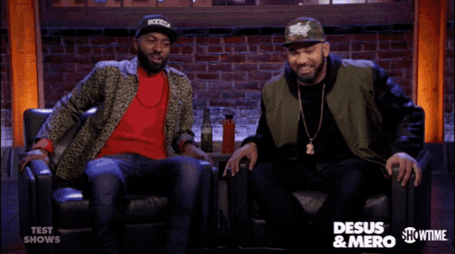 two men are sitting on a couch in front of a sign that says desus & mero