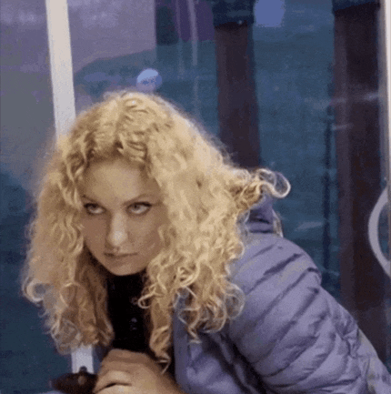 a woman with curly blonde hair wearing a purple jacket looks at the camera