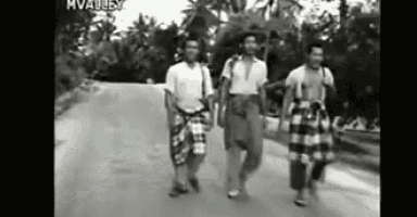 a group of men are walking down a dirt road in a black and white photo .