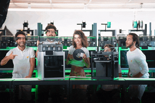 a group of people are standing around a table with a 3d printer