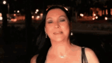 a woman wearing a necklace and earrings is standing in front of a car