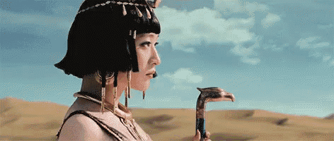 a woman dressed as a pharaoh is holding a snake in the desert .