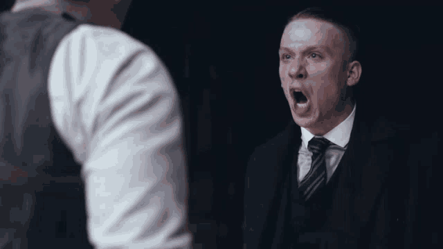 a man in a suit and tie shouts at another man