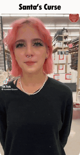 a woman with pink hair is wearing a black sweater and pearls