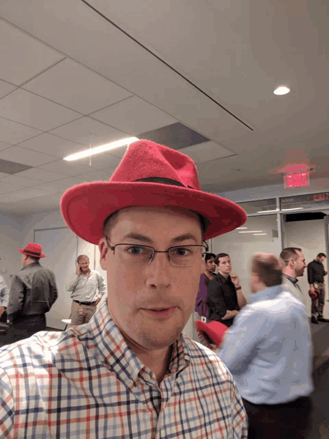 a man wearing a red hat and glasses stands in front of a group of men