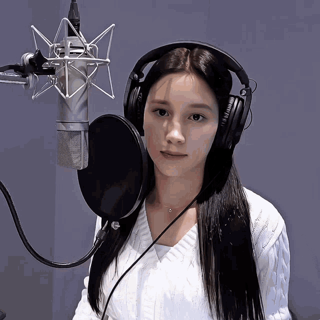 a woman wearing headphones stands in front of a microphone and looks at the camera