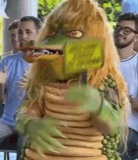 a man in a monster costume is holding a hot dog in his mouth in front of a crowd of people