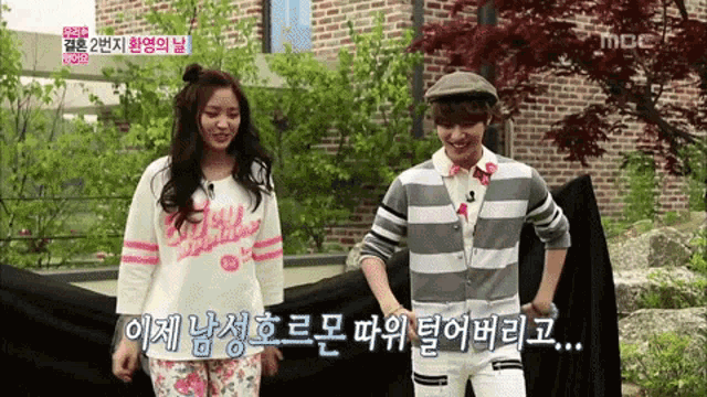 a man and a woman are standing in front of a brick building with a mbc logo on the bottom right