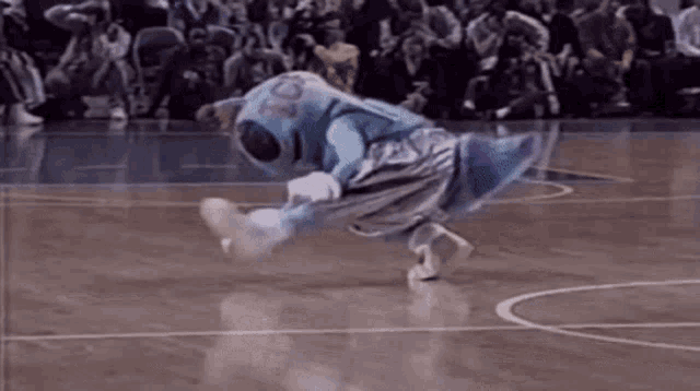 a mascot is doing a trick on a basketball court while a crowd watches .