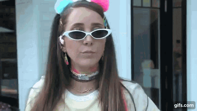 a woman wearing sunglasses and a colorful headband is standing in front of a white building .