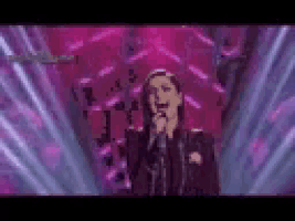 a woman is singing into a microphone on a stage in front of a purple background .