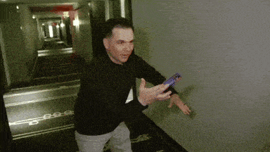 a man is holding a cell phone in a hallway with the number 25 on the wall