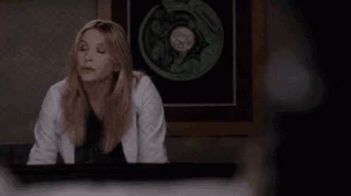 a woman in a lab coat is sitting at a desk in front of a picture on a wall .