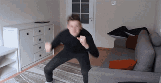 a man in a black shirt is squatting in front of a gray couch
