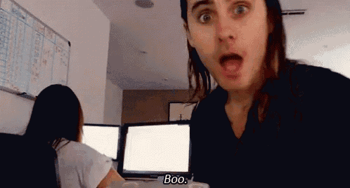a man with long hair is standing in front of a woman and says boo .