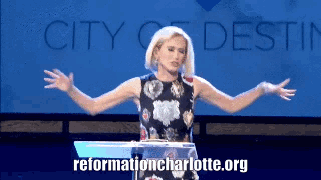 a woman stands at a podium with her arms outstretched in front of a city of destiny banner